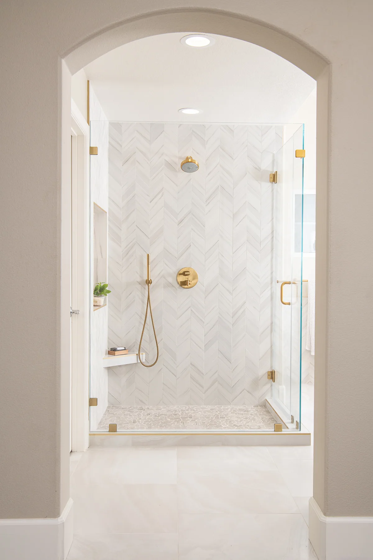 Arched opening leading into a herringbone marble walk-in shower in a Suwanee, GA primary bath