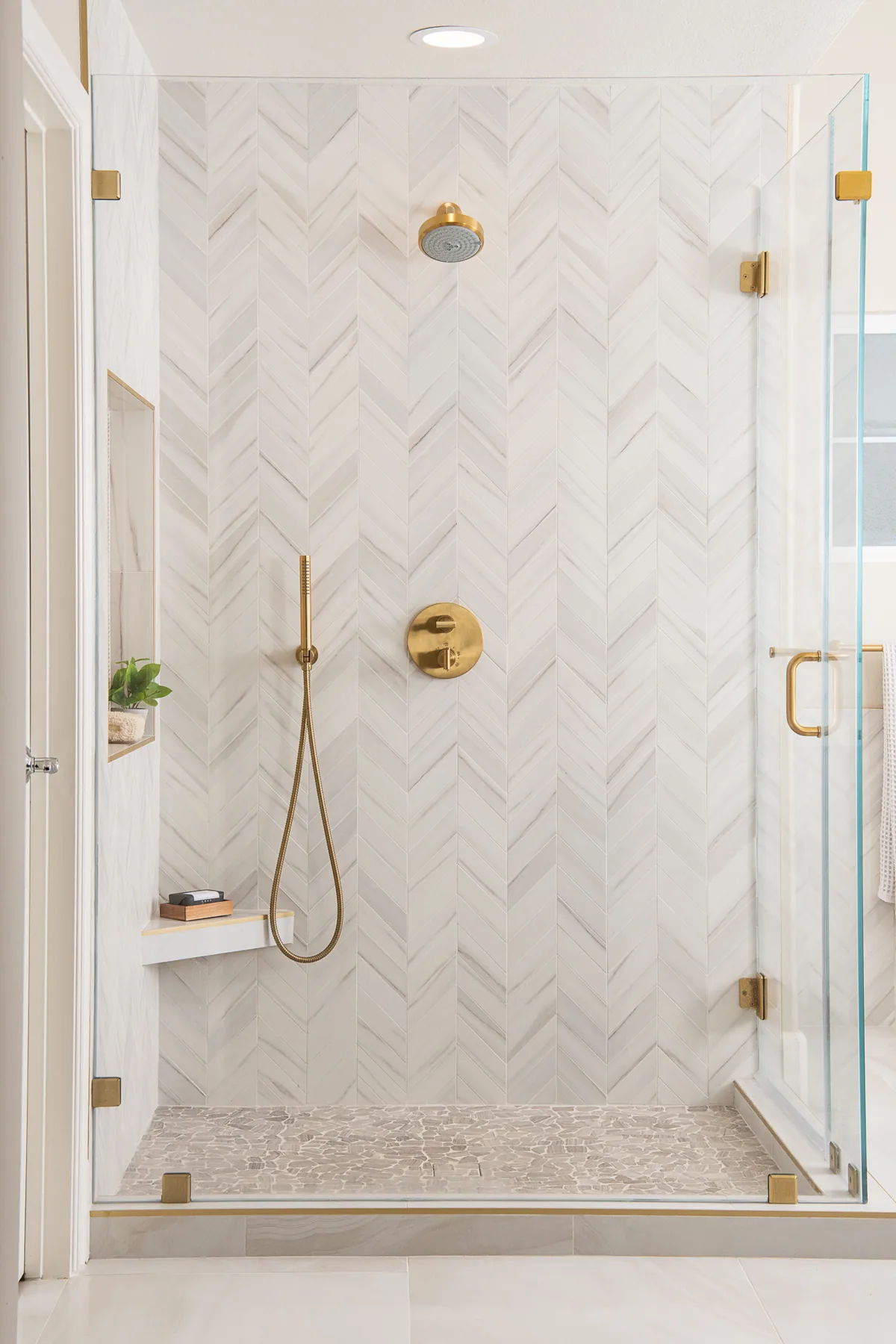 Herringbone marble walk-in shower with brass fixtures and frameless glass in Gwinnett County