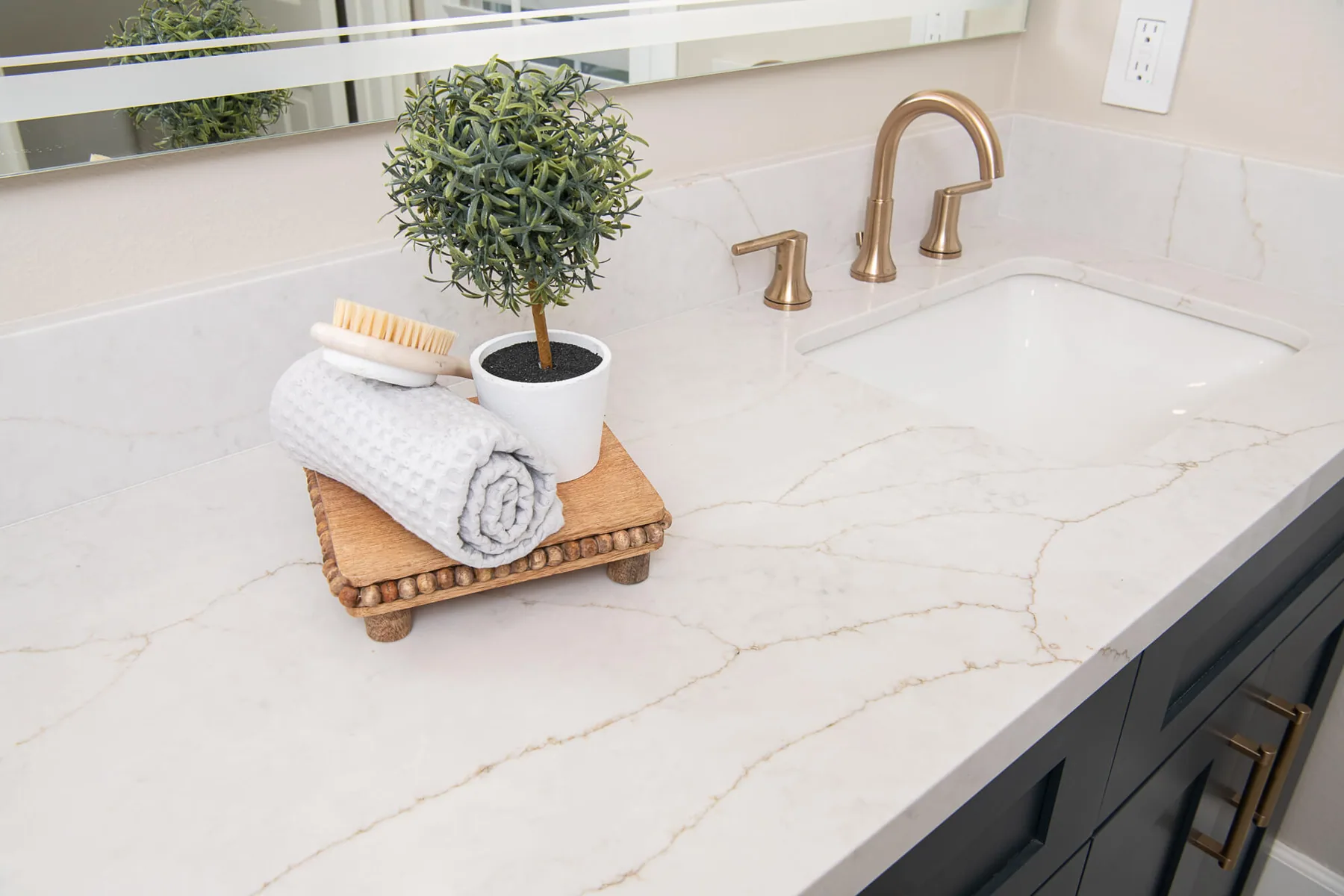 Veined quartz countertop and brushed brass faucet on a navy vanity in a Peachtree Corners, GA bathroom
