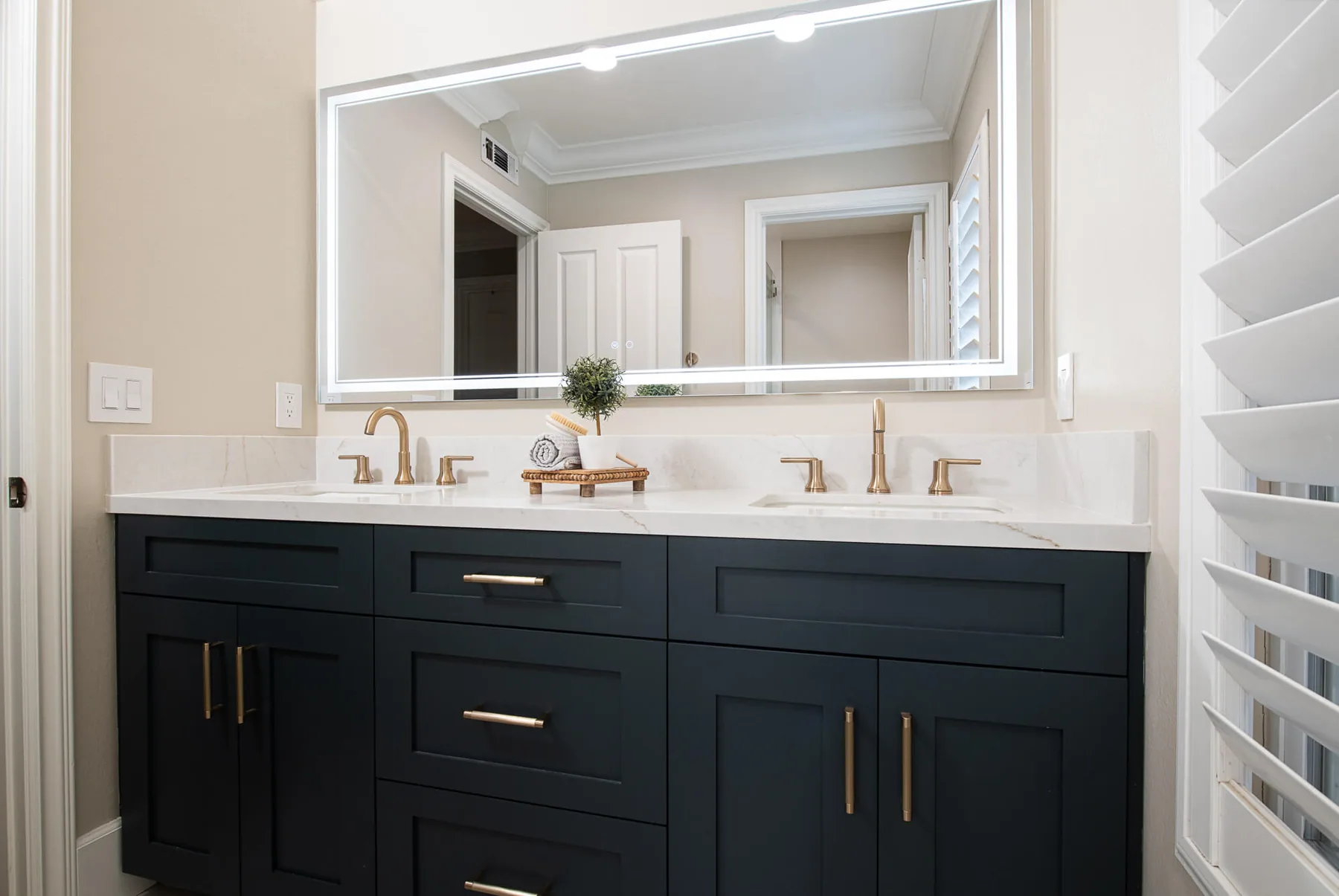 Navy double vanity with a backlit mirror and brass faucets in a Gwinnett County bathroom